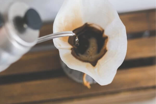 imagem de água sendo colocada em um filtro com pó de café dentro dele passando o café para um recipiente