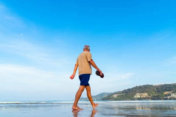 imagem de um jovem senhor caminhando na areia da praia com o chinelo na mão