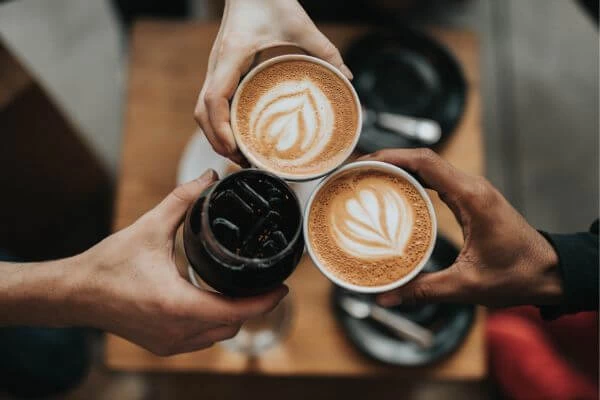 imagem de mãos de três pessoas cada uma com uma xícara de café e brindando