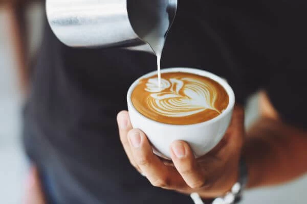 imagem de um barista segurando uma xícara branca de café e usando leite para desenhar nele